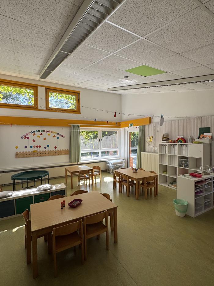 Heller Gruppenraum mit Tisch, Stühlen und Regalen